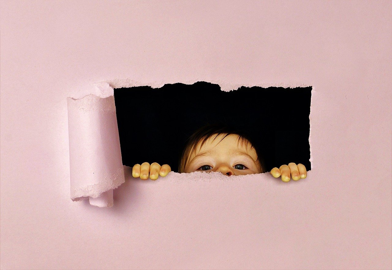 Ein Kind steht auf Zehenspitzen und streckt seinen Kopf durch ein Loch in der Tapete.